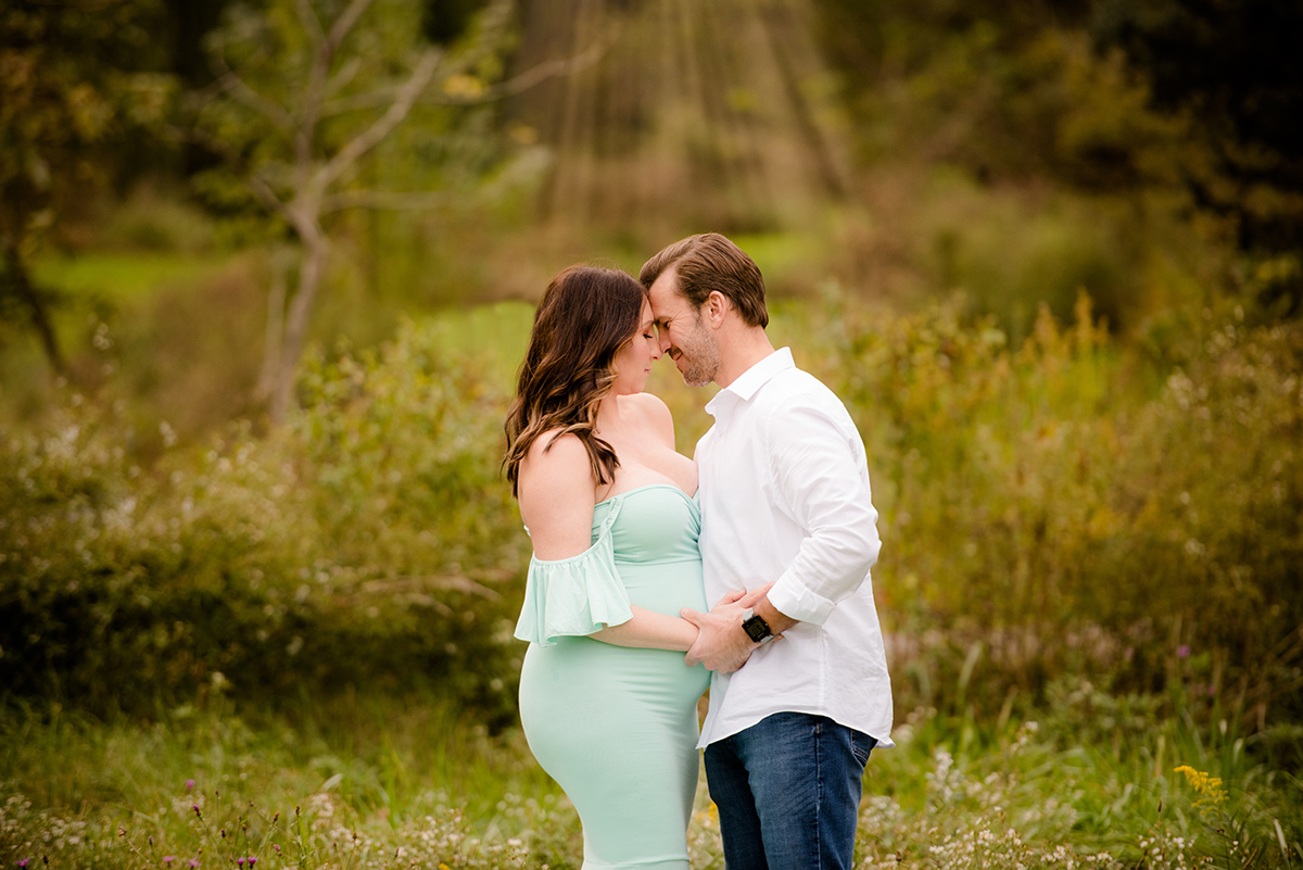 pregnant couple kissing in field