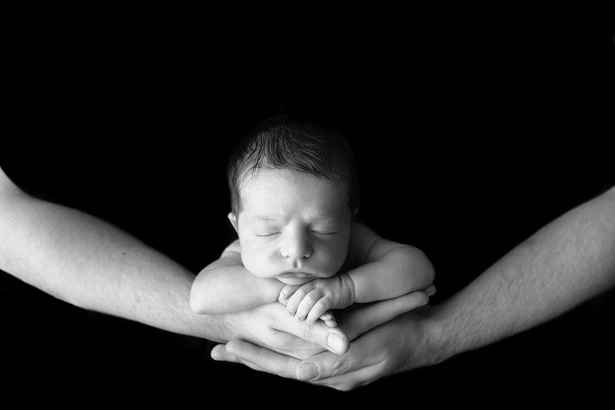 black and white image of newborn in dads hands