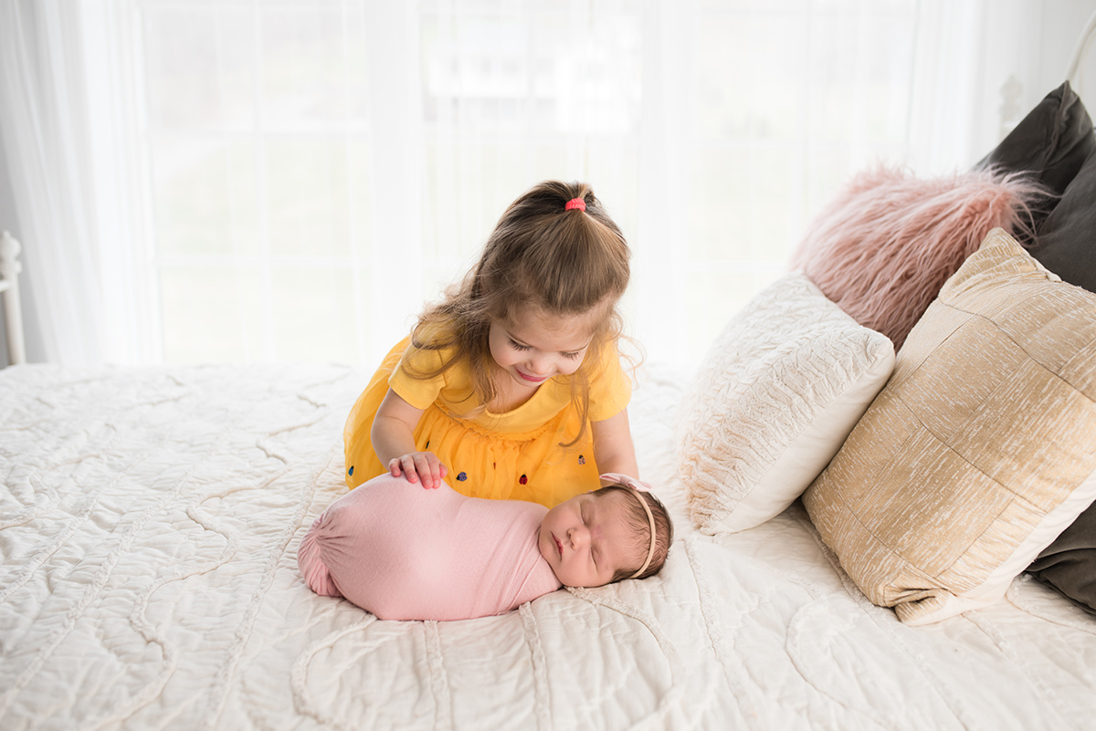 toddler looking at newborn on a bed