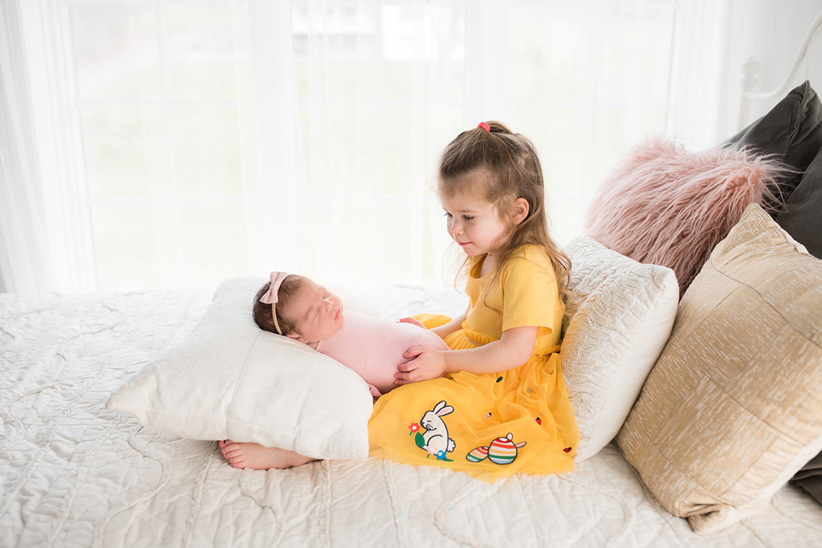 Toddler holding newborn on bed